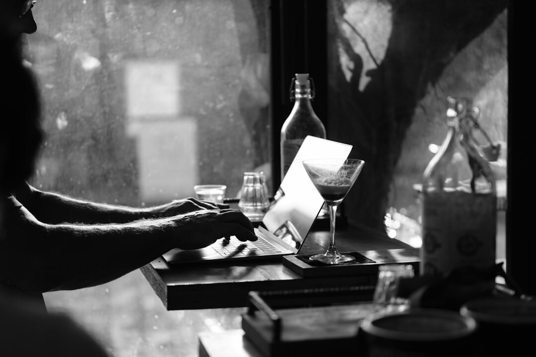 Hands editing black and white documentary photographs on a laptop next to printed contact sheets